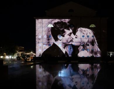 Projection of a kiss on a building at night.