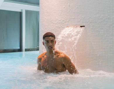 Homme dans une piscine sous une cascade.