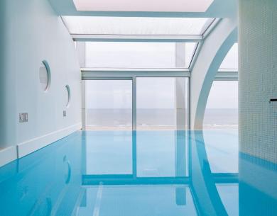 Piscine intérieure avec vue sur la mer et grandes fenêtres.