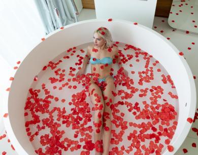 Woman in tub with rose petals and fireplace.