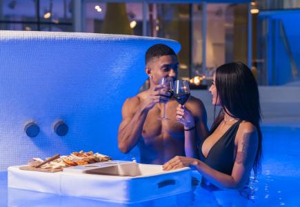 Couple toasts in pool with wine and snacks.