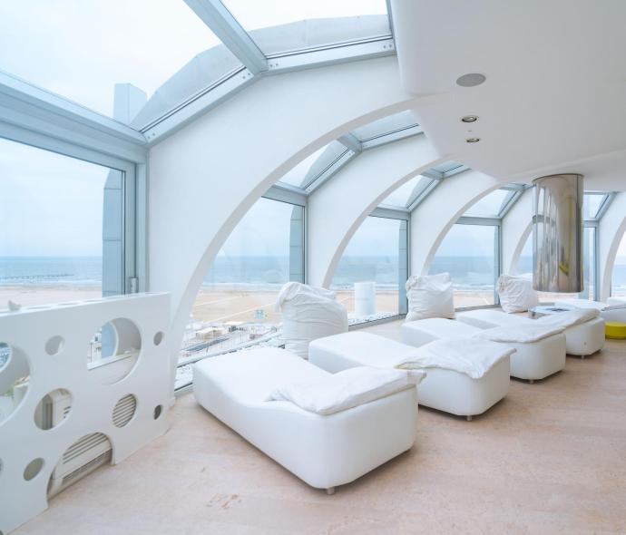 Salle de détente avec vue sur la mer et chaises longues blanches.