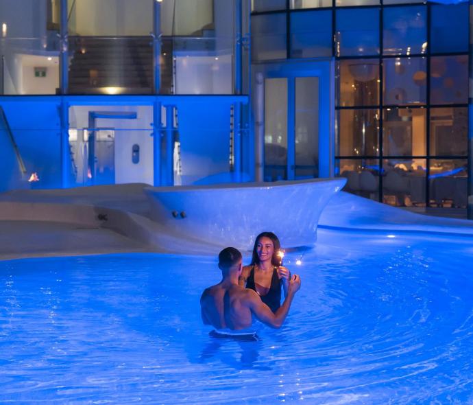 Coppia in piscina con luci blu, atmosfera romantica.