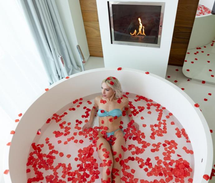 Woman in tub with rose petals and fireplace.